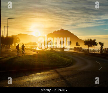 Die Sonne hinter dem Monte Urgull von San Sebastian, Baskenland, Guipuzcoa. Spanien. Blick vom Strand Zurriola Avenue. Stockfoto