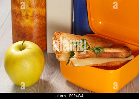 Gelbe sandwich Box mit gerösteten Scheiben Brot, Käse und Petersilie Grün, grüner Apfel und gebundene Bücher auf dem Hintergrund. Schule Frühstück. Stockfoto