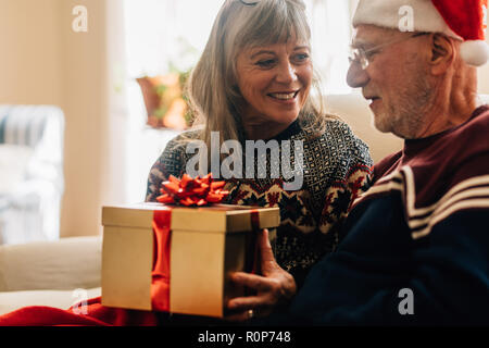 Ältere Frau ein Geschenk zu ihrem Mann zu Weihnachten. Senior Paar den Austausch von Geschenken Weihnachten zu Hause feiern. Stockfoto