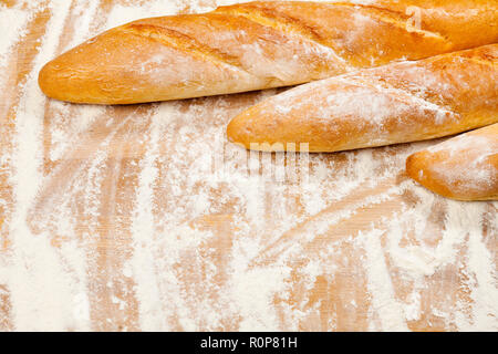Frisch gebackene handwerklichen Baguettes (französisches Brot) auf Holz- Hintergrund mit Mehl Stockfoto