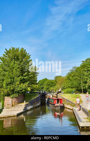Ein rot lackiert Lastkahn auf dem Kennet und Avon Kanal mit Menschen auf der Suche nur auf, nachdem er durch ein Schloss an einem sonnigen Tag, Newbury, Berkshire, Großbritannien Stockfoto