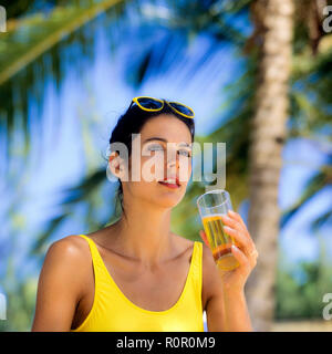 Junge Frau mit gelben Badeanzug mit einem Glas Bier, Palmen Hintergrund, Guadeloupe, Französisch Westindien, Stockfoto