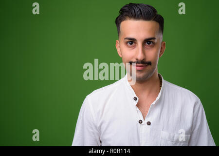 Junge hübsche Iranische Mann mit Schnurrbart gegen grüne backgroun Stockfoto