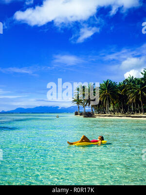 Junge Frau in Rot Badeanzug Sonnen auf gelb Luftmatratze, schwimmend auf Karibische Meer, tropische Strand, Palmen, Guadeloupe, Französisch Westindien, Stockfoto