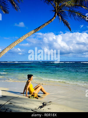 Junge Frau mit gelben Badeanzug sitzen auf tropischen Strand, Palmen, Karibik, Guadeloupe, Französisch Westindien, Stockfoto