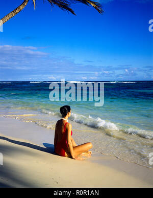 Junge Frau mit roten Badeanzug sitzen auf tropischen Strand und mit Blick auf das Karibische Meer, Guadeloupe, Französisch Westindien, Stockfoto