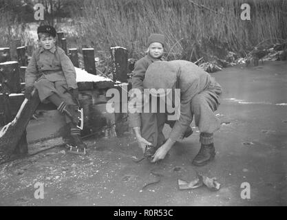 1930er Jahre Aktivitäten im Winter. Ein Vater seinen Kindern hilft, ihre Schlittschuhe auf ihre Schuhe zu passen. Die Schlittschuhe sind der einfachsten König mit nur einer metallkante ist auf die Schuhe der Kinder ausgestattet. 26.November 1939. Schweden Foto Kristoffersson ref 17-7 Stockfoto