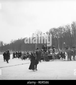 Eiskunstlauf um die Jahrhundertwende 1800-1900. Ein paar zusammen abgebildet beim Eislaufen im Freien. Im Hintergrund eine typische Schaukel Schlitten mit Kindern spielen. Bild wahrscheinlich auf einen Film. Schweden 1952. Foto Kristoffersson ref BF 51-8 Stockfoto