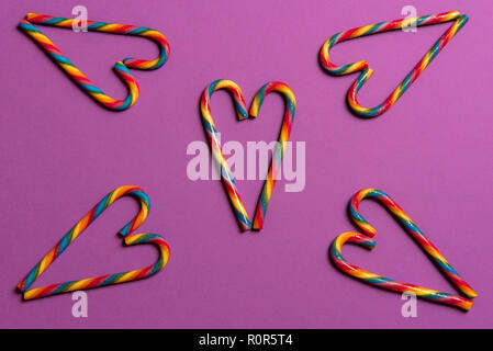 Oben Ansicht von Rainbow bunte Zuckerstangen in Herzform auf lila Papier Hintergrund angeordnet. Minimalistische Weihnachten Konzept. Stockfoto