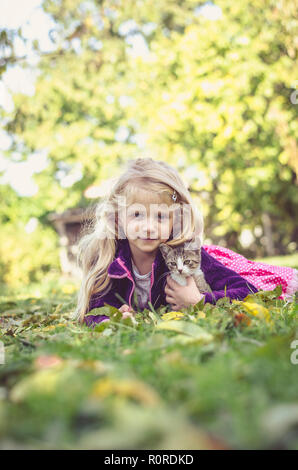 Schöne blonde Mädchen mit Katze und zusammen liegen auf Gras im Herbst Stockfoto