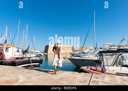 Reisen touristische Frau auf Urlaub in Heraklion Kreta Wandern am Hafen. Schöne elegante Mädchen in beige Kleid Besuch der berühmten mediterranen Venet Stockfoto