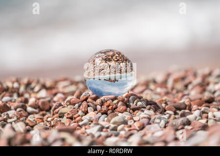 Historische Altstadt in Sveti Stefan große transparente Glas Kugel spiegelt sich auf Peebles am Strand, Küste von Montenegro Stockfoto
