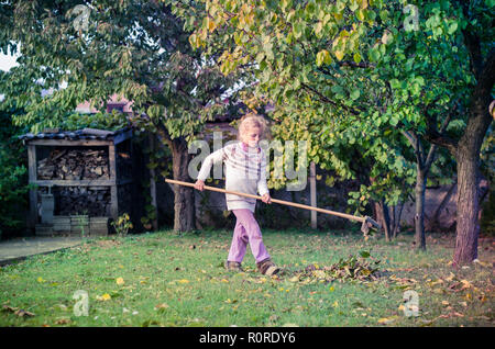 Kind harken gefallen Herbstliche Blätter im Garten Stockfoto