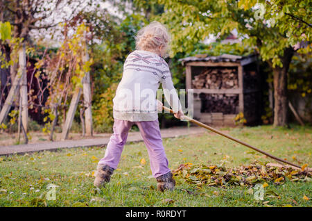 Kind harken gefallen Herbstliche Blätter im Garten Stockfoto