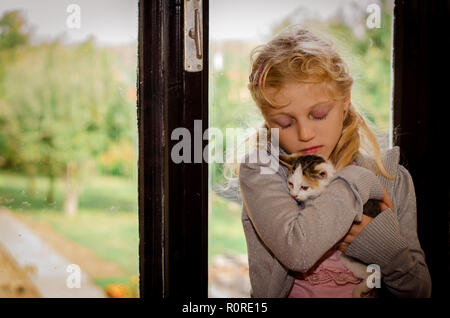 Schöne blonde Mädchen sitzt am Fenster und Halten einer Katze Stockfoto