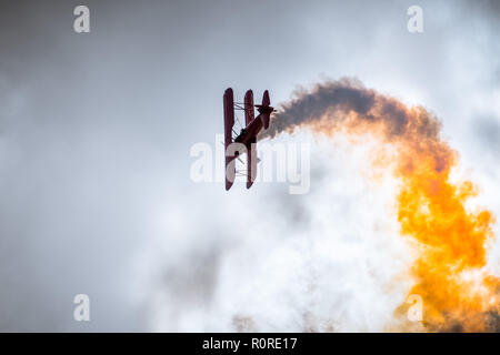 Alte Flugzeug performing flying Tricks und hinterlässt eine Spur der bunten Rauch; bewölkter Himmel Hintergrund Stockfoto