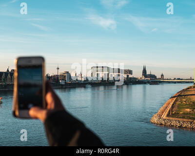 Junge Frau, die Bilder von der Skyline von Köln mit ihrem Smartphone Stockfoto