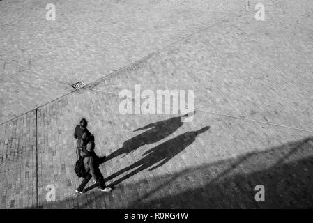 Verschwommen unkenntlich Paar von oben zu Fuß auf einem offenen Raum Platz mit Schatten projizieren auf dem Boden Stockfoto