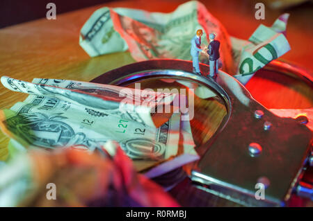 Konzeptuelle Miniatur kriminelle Geschäftsleute Hände schütteln auf Handschellen mit Zerknüllter Dollarnoten und Polizei Lichter Stockfoto