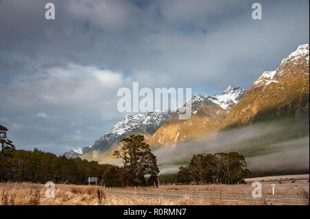 Sonnenaufgang im Fjordland, Neuseeland. Nebel Hängen über dem Tal, mit schneebedeckten Bergen und bewölkter Himmel Hintergrund. Stockfoto