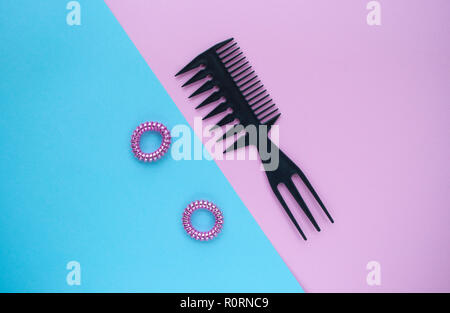 Kunststoff schwarz Kamm und zwei rosa glänzenden scrunchies auf Pastell rosa und blauen Hintergrund. Stockfoto