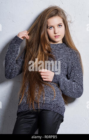 Mode Teenager stehendes Mädchen lehnte sich zurück gegen einen weißen Betonwand. Stilvolle attraktive hipster Girl 12 Jahre Hand heben Haar Holding posieren. Schönes Modell. Serie von Fotos. Stockfoto