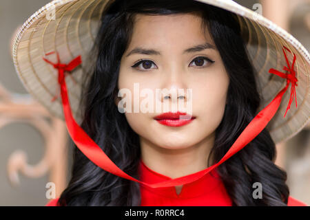 Hübsche junge vietnamesische Frau im roten top mit passendem Lippenstift tragen Strohhut, Nahaufnahme, Gesicht Porträt der Blick in die Kamera Stockfoto