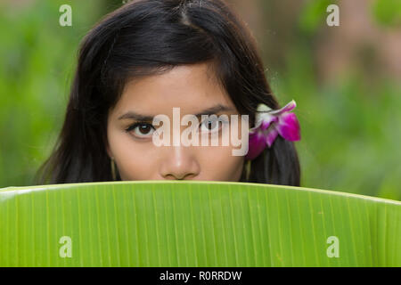 Portrait einer jungen Vietnamesin peeking über der Oberseite eines banana tree Blatt an der Kamera Stockfoto