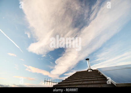 Hohe Wolken und Kondensstreifen auf Ambleside, Lake District, England mit einem Haus Dach mit Solarzellen. Stockfoto