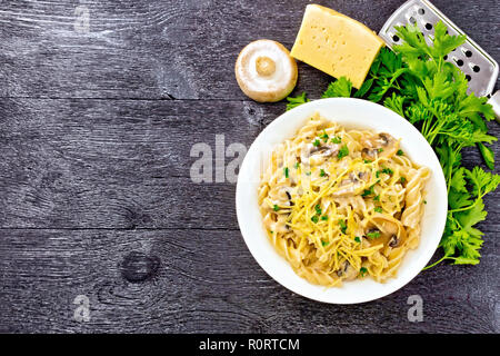 Fusilli mit Champignons in Rahmsauce, Petersilie und geriebenem Käse in einer Platte auf Holzbrett Hintergrund von oben Stockfoto