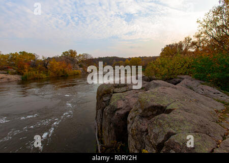 Dunkle schnell fliessenden Fluss durch gelbe Herbst Bäume umgeben auf der felsigen Ufer Stockfoto