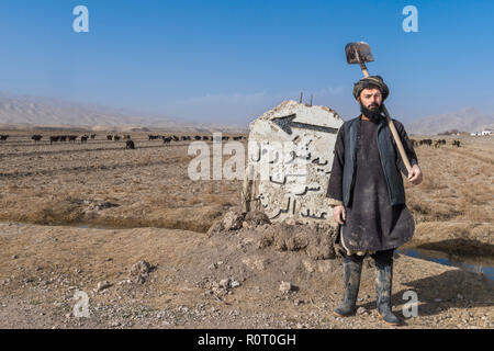 Einsamer Bauer mit Spaten Vor Beschilderung unter der Dürre auf der Straße von Kholm, Takht-e Rostam, Provinz Samangan, Afghanistan Stockfoto