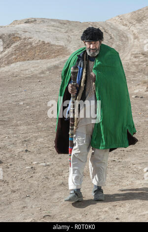 Alten Sufi Mann mit grünen Mantel Wandern in der Wüste mit Stock in Richtung Haschisch Rauchen Höhle, Alte Balkh im Norden Afghanistans Stockfoto