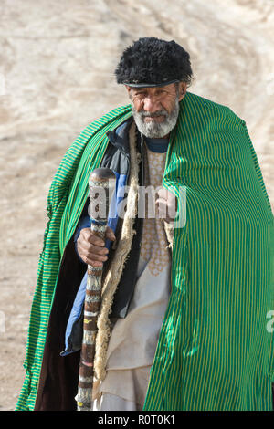 Alten Sufi Mann mit grünen Mantel Wandern in der Wüste mit Stock in Richtung Haschisch Rauchen Höhle, Alte Balkh im Norden Afghanistans Stockfoto