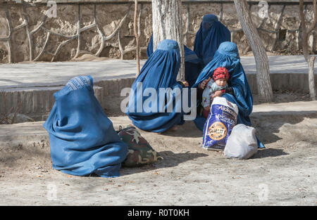 Drei Frauen und ein Kind tragen traditionelle Blaue Burka Entspannen in einem Park auf dem Boden sitzend mit Tasche, Mazar-e Sharif, Provinz Balkh, Afghanistan Stockfoto