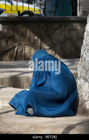 Müde Frau mit traditionellen blauen Burka Entspannen in einem Park sitzen auf dem Boden und lehnte sich an einen Baum, Mazar-e Sharif, Provinz Balkh, Afghanistan Stockfoto