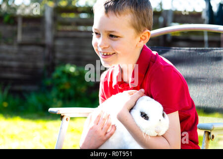 Ein schöner Glücklich lächelnde Junge mit Autismus, Asperger-syndrom und adhd Kuscheln sein liebstes Haustier Kaninchen im Garten zu Hause Stockfoto