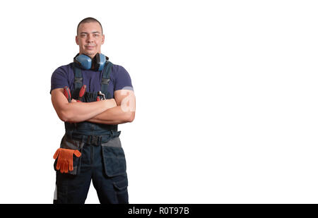 Starke männliche Mechaniker in Blau overal stehend mit orange Handschuhe, weißen Helm, Gehörschutz und Tools auf einem weißen Hintergrund isoliert Stockfoto