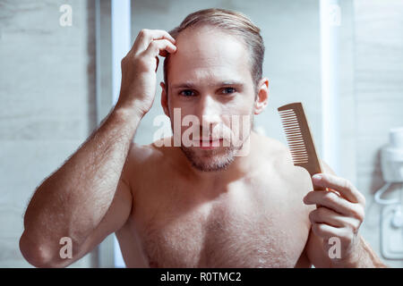 Blauäugigen Mann seine nassen Haare kämmen nach dem Waschen in der Dusche Stockfoto