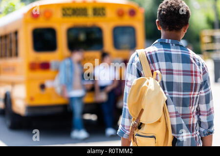 Ansicht der Rückseite des afrikanischen amerikanischen Schüler zu Fuß zu Klassenkameraden lehnte sich auf School Bus Stockfoto