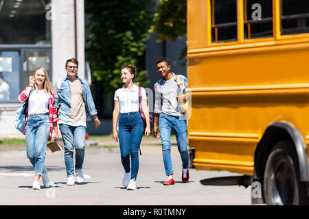 Gruppe von jugendlich Gelehrten zu Fuß hinter dem Schulbus auf Parkplatz Stockfoto