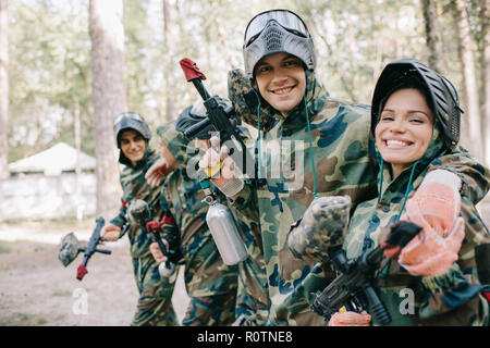 Lächelnden jungen männlichen, weiblichen paintballer Mannschaftskamerad in Camouflage mit Paintball gun im Freien Stockfoto