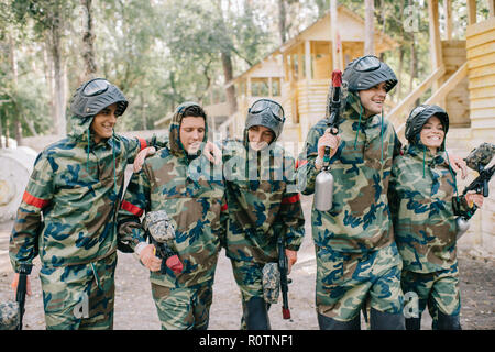 Lachend paintball Spieler in Camouflage mit Marker Gewehren umarmen einander im Freien Stockfoto