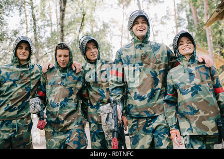 Gerne paintball Spieler in Camouflage mit Marker Gewehren umarmen einander im Freien Stockfoto