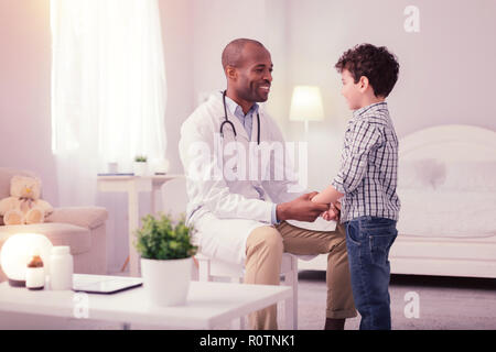 Frohe freundlichen Arzt seine Patienten in der Hand halten Stockfoto