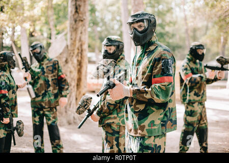 Paintball Team in Uniform und Schutzmasken spielen paintball mit Marker Gewehren im Freien Stockfoto