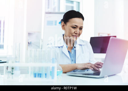 Freudige positive Frau vor dem Laptop sitzen Stockfoto