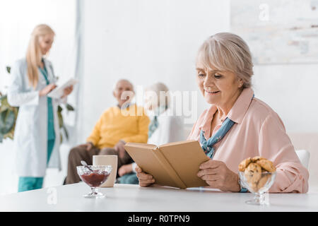 Ältere Frau mit Buch, während die weiblichen Arzt Untersuchung Menschen Stockfoto