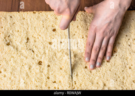 Schneiden Biskuitboden auf lagen. Vorbereitung einer Torte Kuchen, Detail der Hände und Messer, close-up Stockfoto