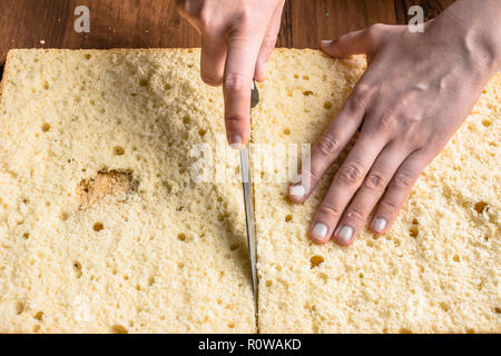 Schneiden Biskuitboden auf lagen. Vorbereitung einer Torte Kuchen, Detail der Hände und Messer, close-up Stockfoto